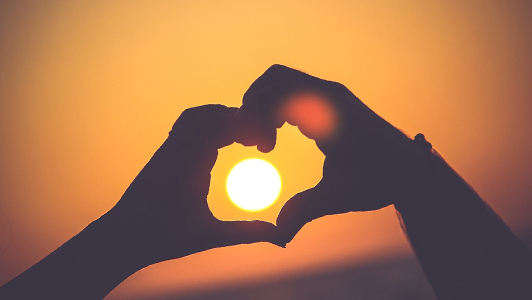 Couple holding hands in a sunset in the shape of heart